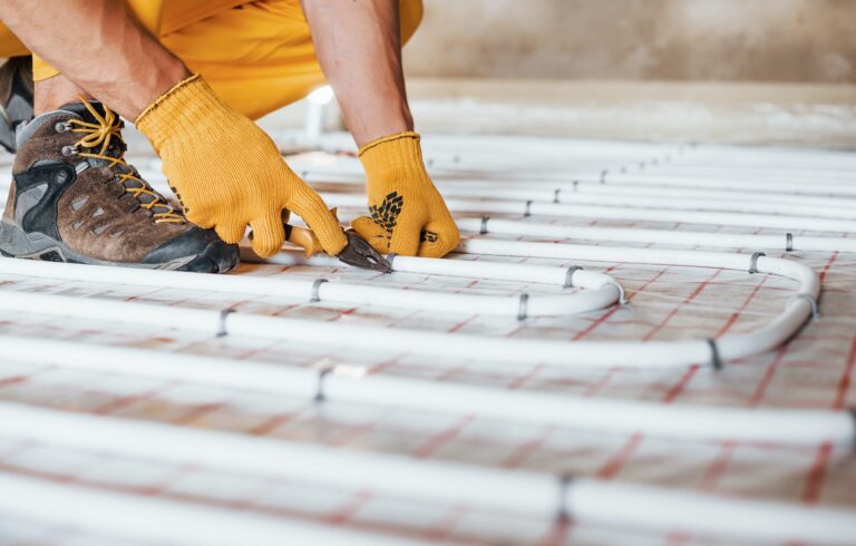 Close up view. Worker in yellow colored uniform installing underfloor heating system